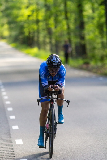 A person wearing a blue bike uniform, riding a bike down the road.