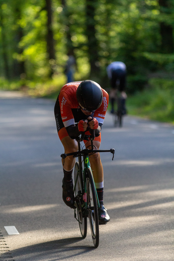 A cyclist in a red jersey with the word Oost on it rides down the street.