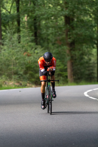 A man in an orange bike racing outfit is riding a bike on the street.