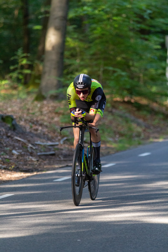 A man in a yellow and black cycling outfit races down a road on his bike.