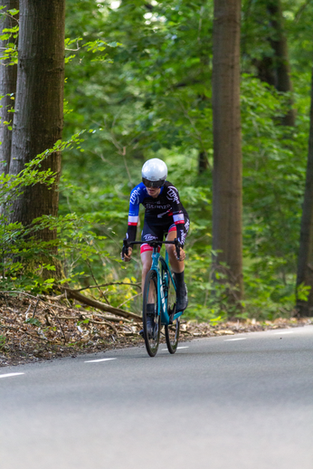 A cyclist on a road wearing blue and black, with the words Cycling Project on their outfit.