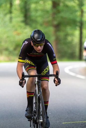 A man on a bike is wearing a black Wielrennen jersey.