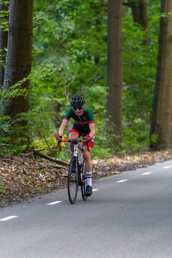 A person riding a bicycle down a forest road, wearing a helmet and matching red and green cycling gear.