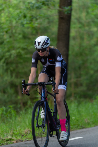 A woman riding a bike through a forest wearing sunglasses and an Eastman Cycling Team shirt.