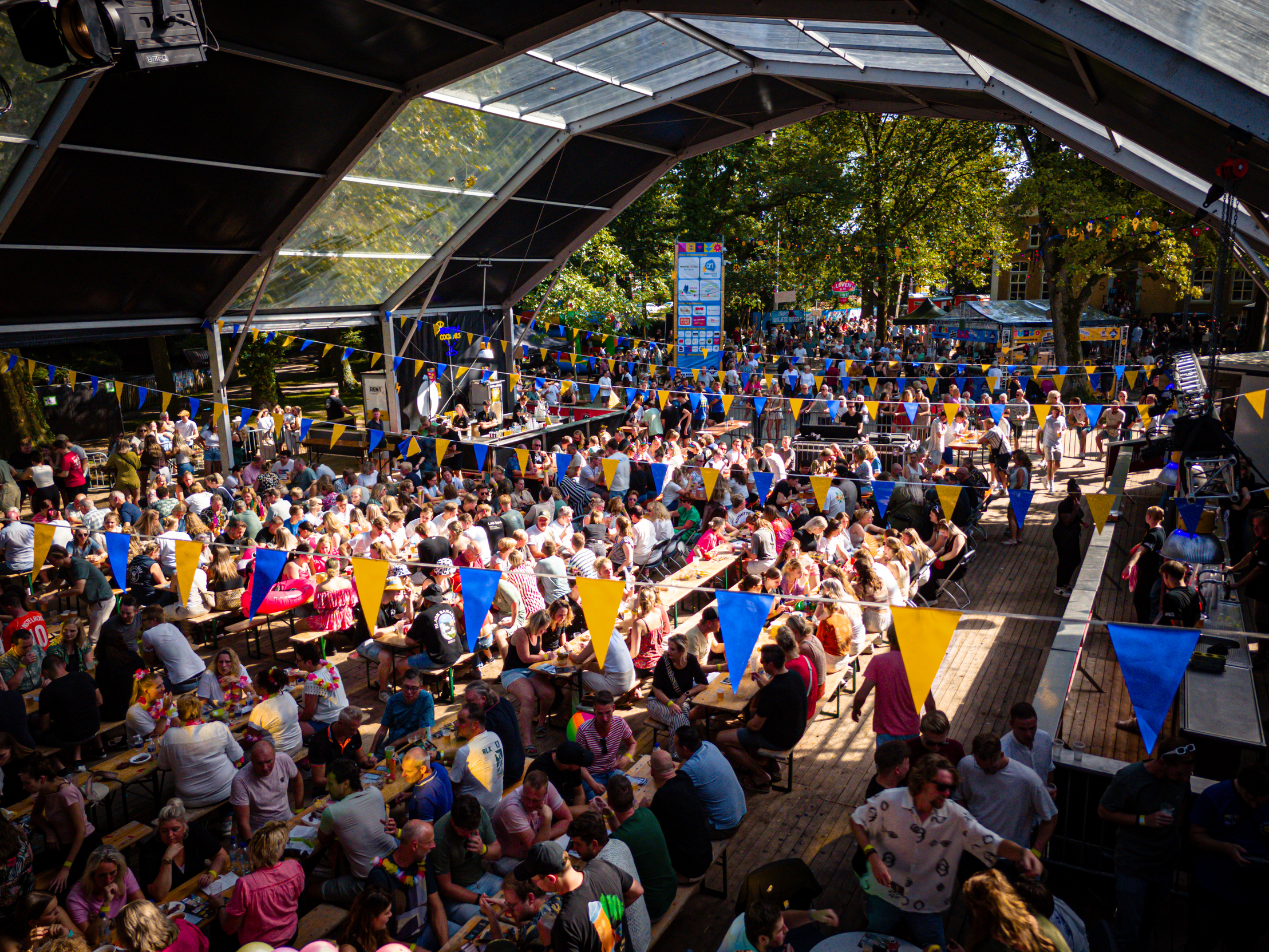 A large crowd gathered at a tented event with blue flags hanging from the rafters.