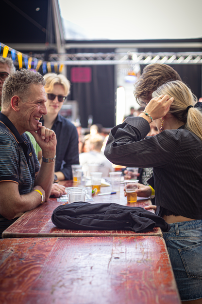 A group of people are gathered around a wooden table, enjoying beers at a bar.