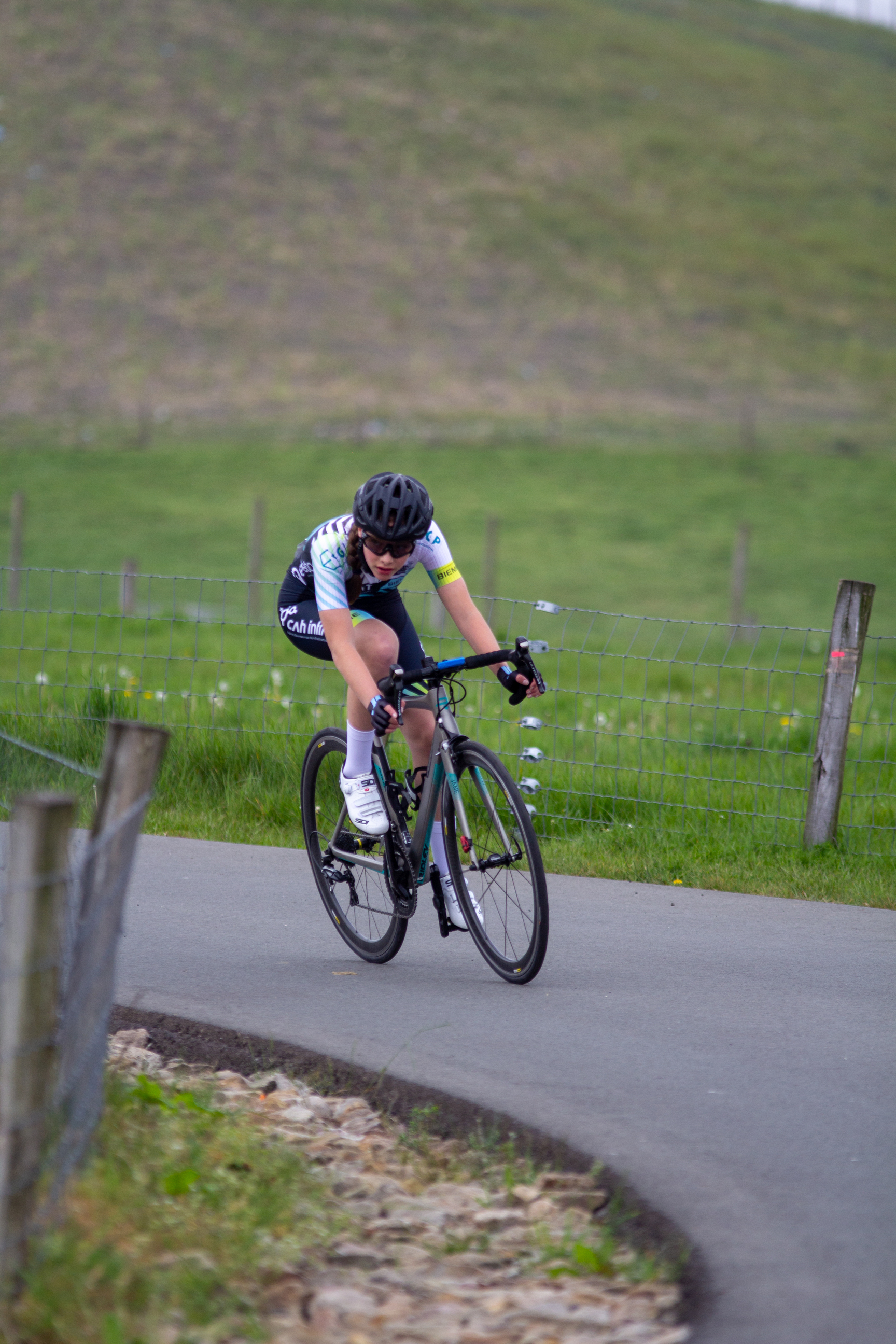 A man wearing a white and blue jersey rides a black bicycle on the side of a road.