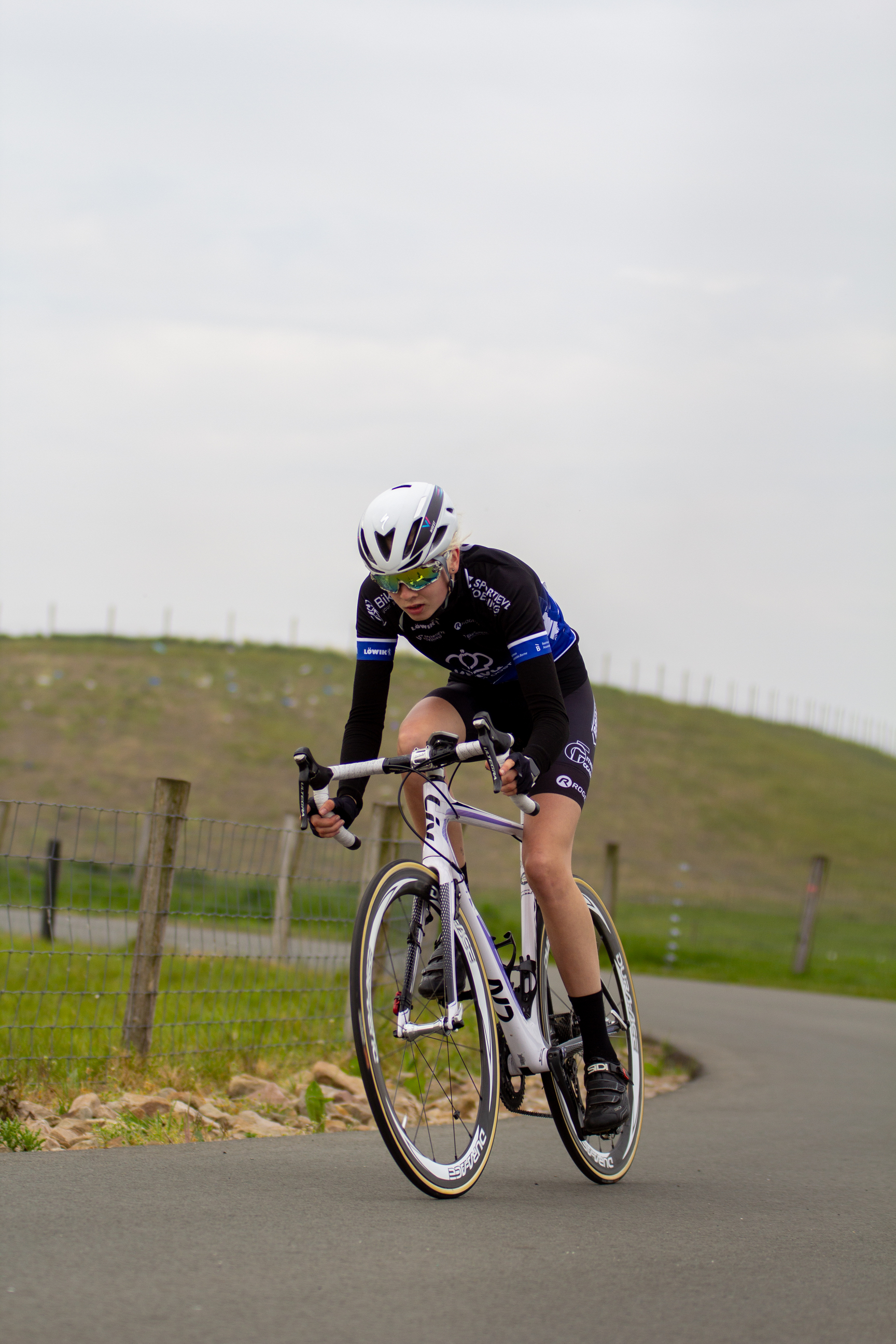 A cyclist wearing a black and blue top is pedaling her bike on the road.