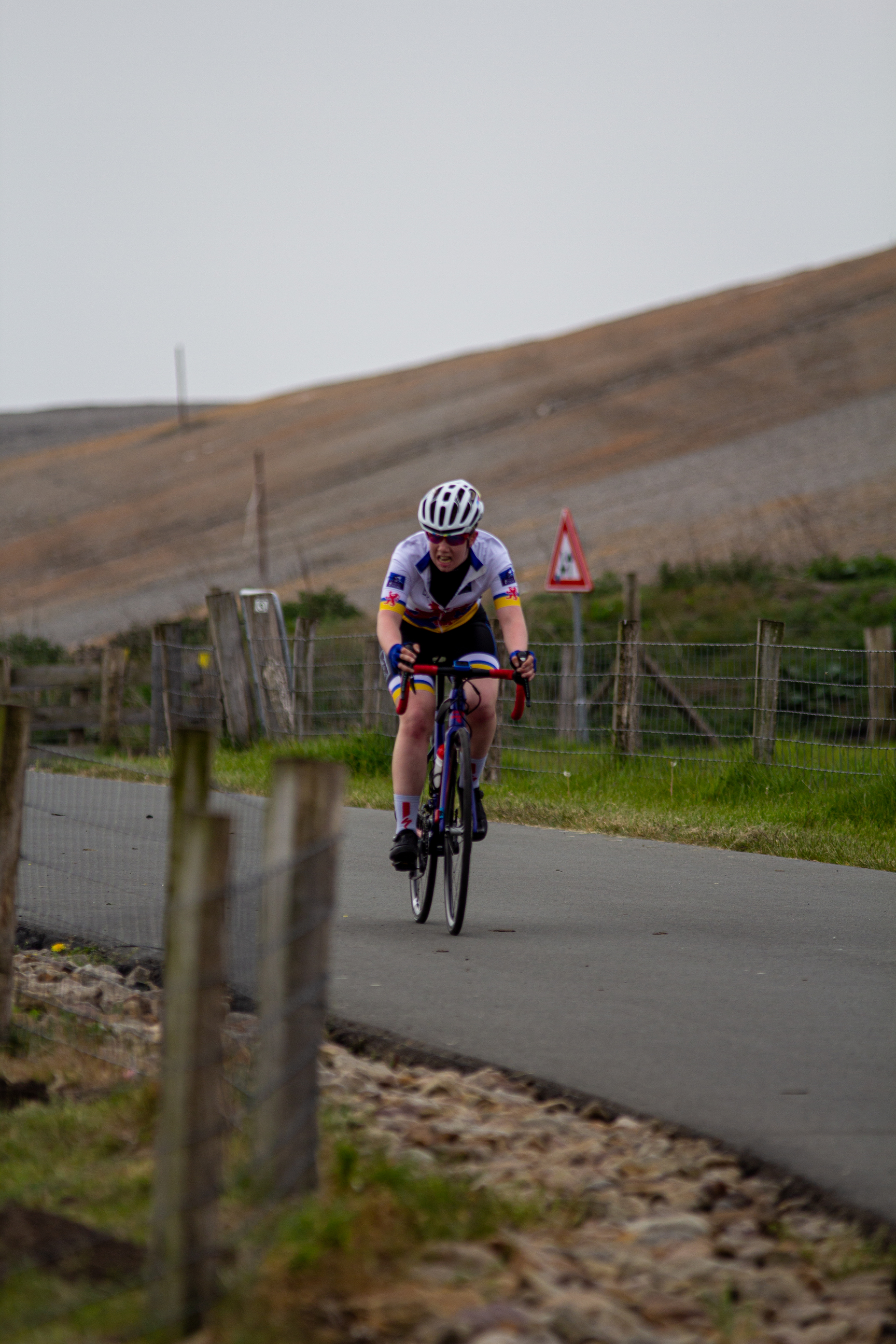 A woman is riding a bicycle on a road, wearing a purple and white outfit.