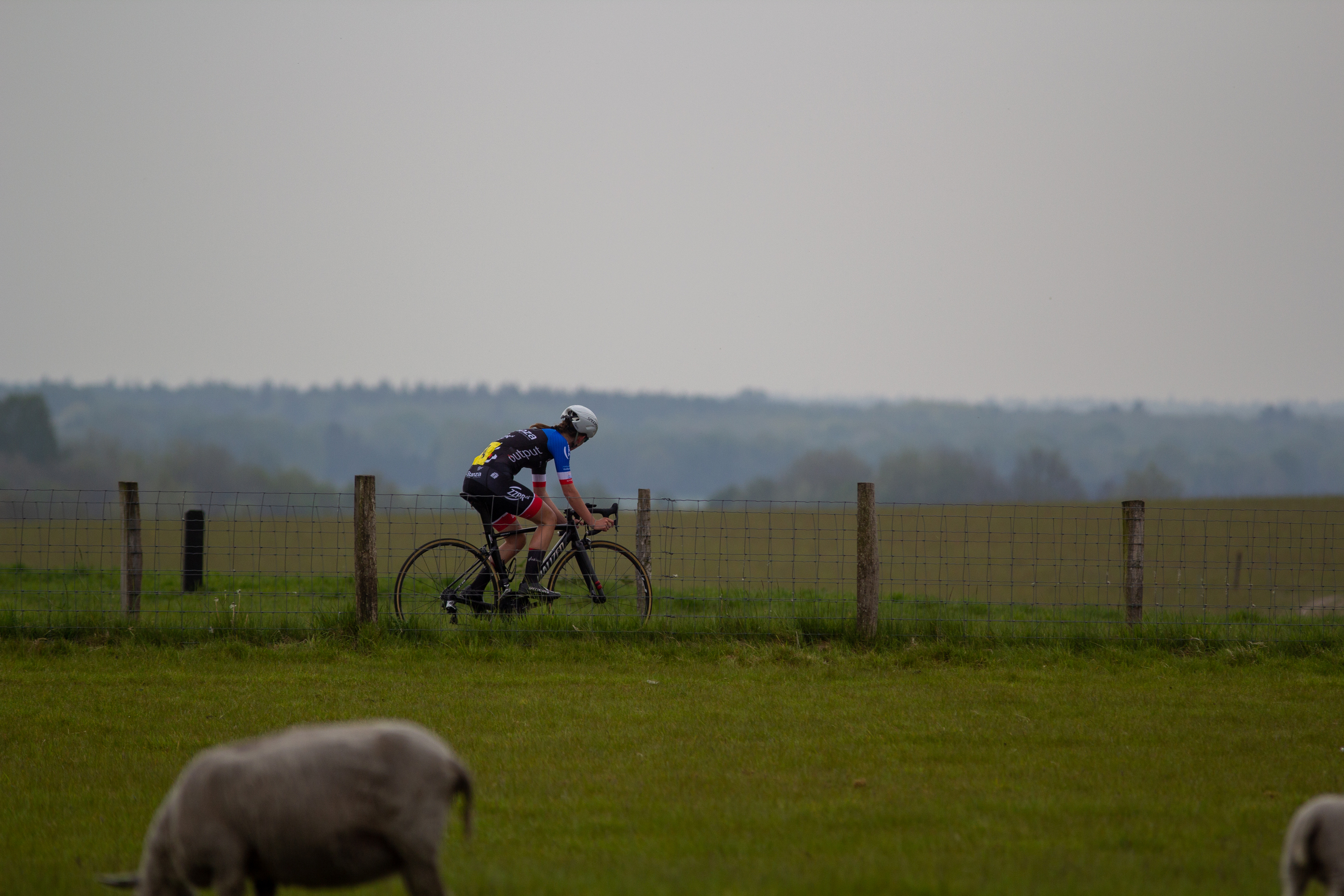 A woman on a bike in the countryside, wearing a black helmet and jersey.