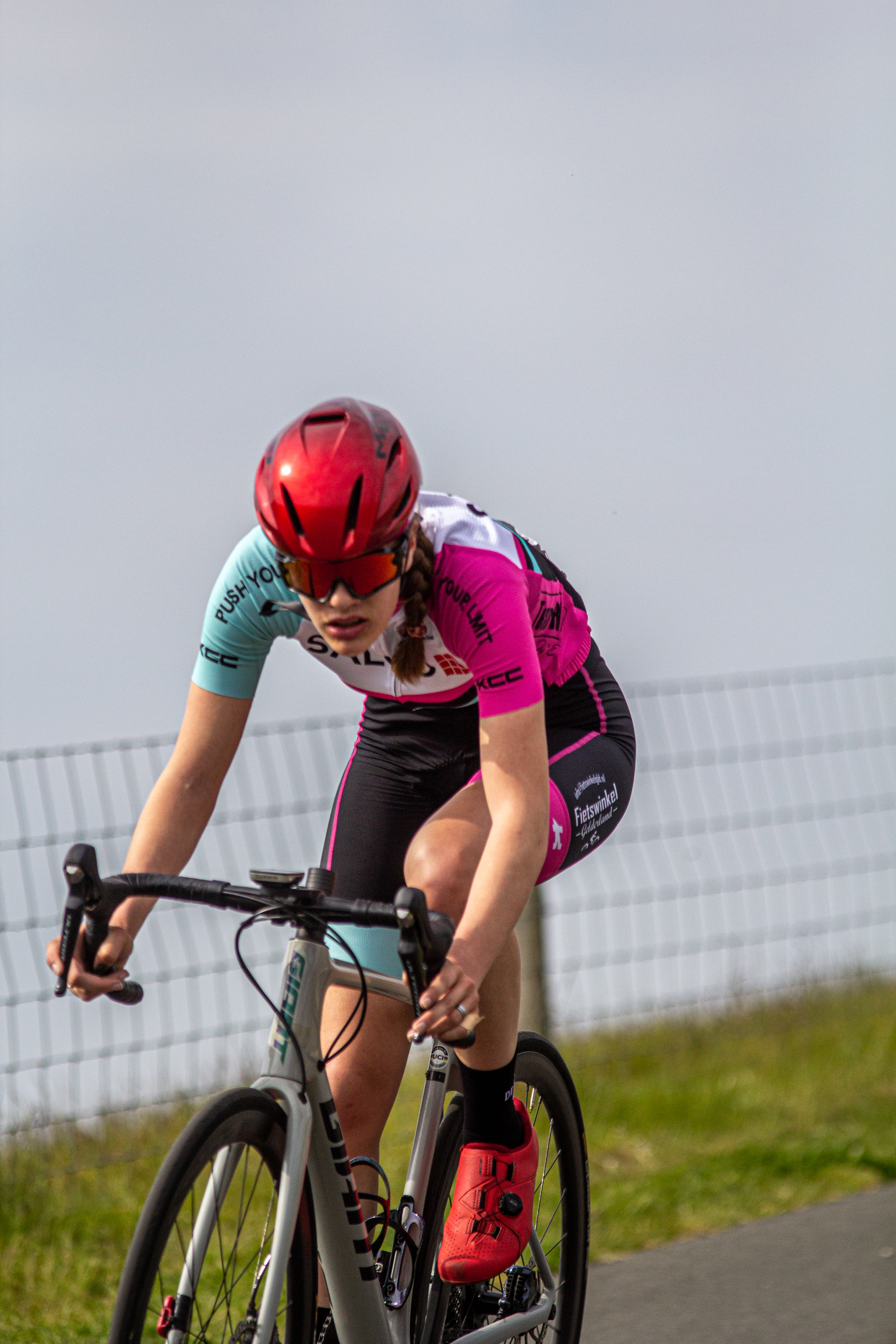 A girl on a bike wearing a pink jersey and a red helmet.