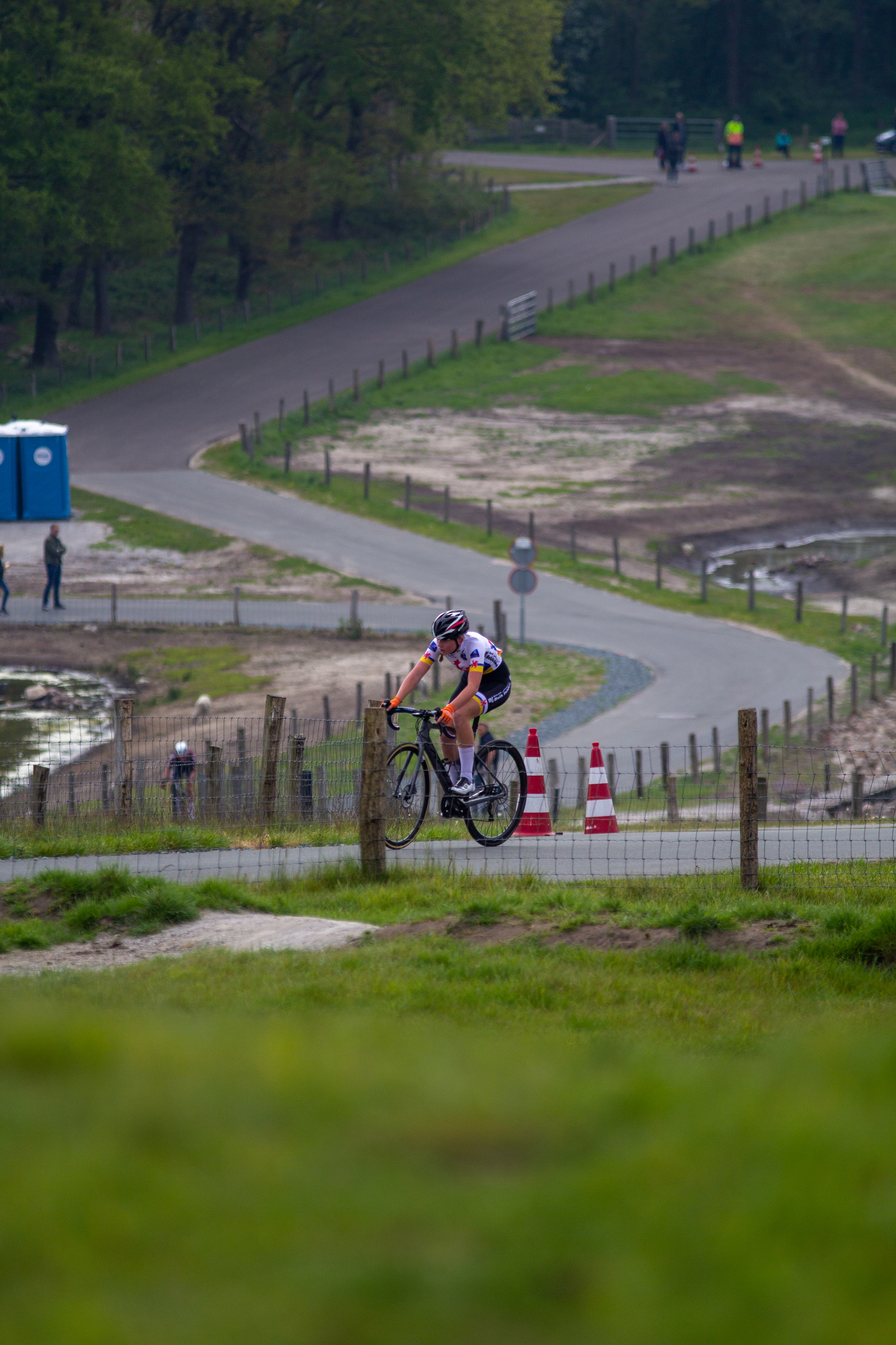 A female bicycle racer on a grassy hill with other racers in the background.