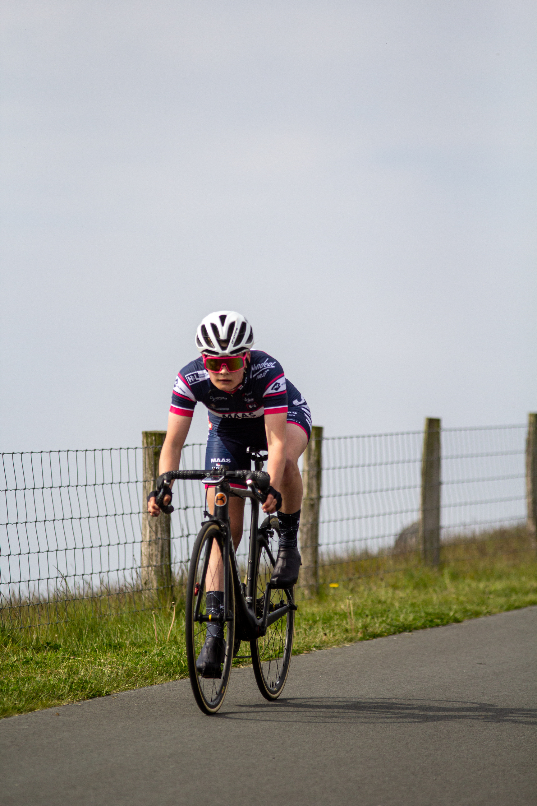 A woman in a black and pink jersey riding her bicycle down the street.