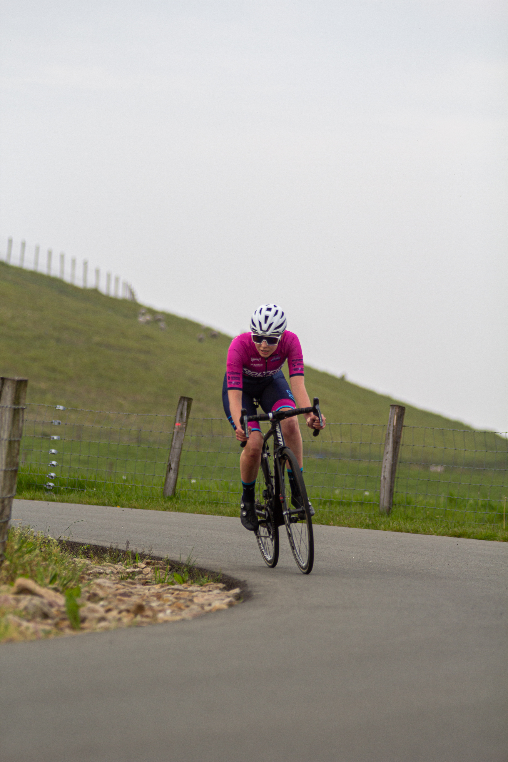 A woman wearing a white and blue helmet is riding a bicycle on the side of a road.