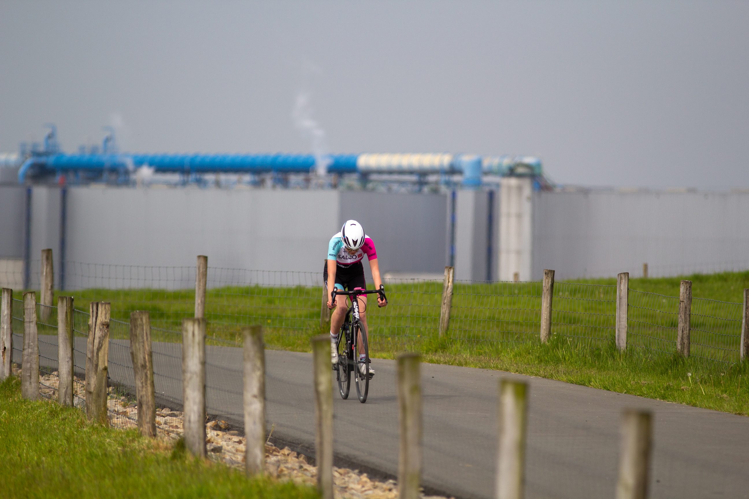 A woman is riding her bike on a road with posts in the foreground.