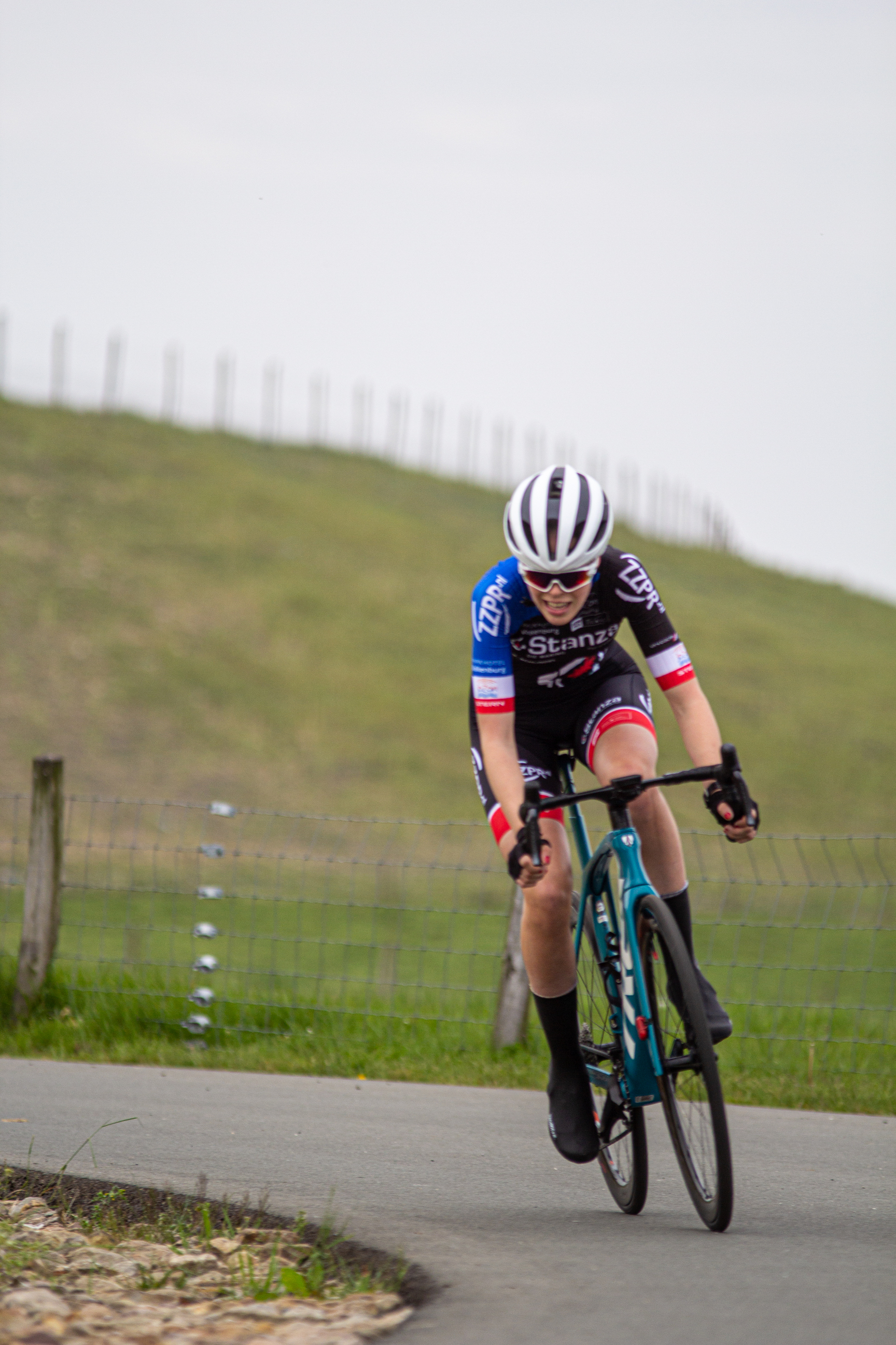 A woman in a black and blue jersey with the word "Sprint" on it is riding her bike down a road.