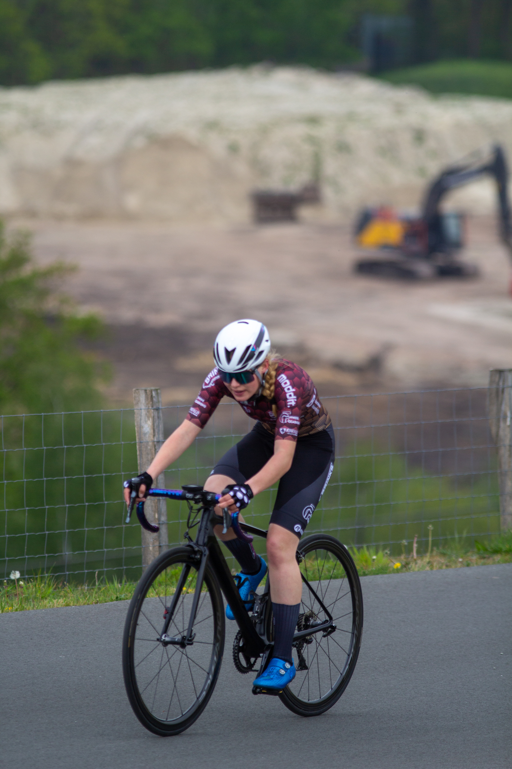 A female cyclist wearing a white helmet with an "X" on the side, riding a black and blue bike.