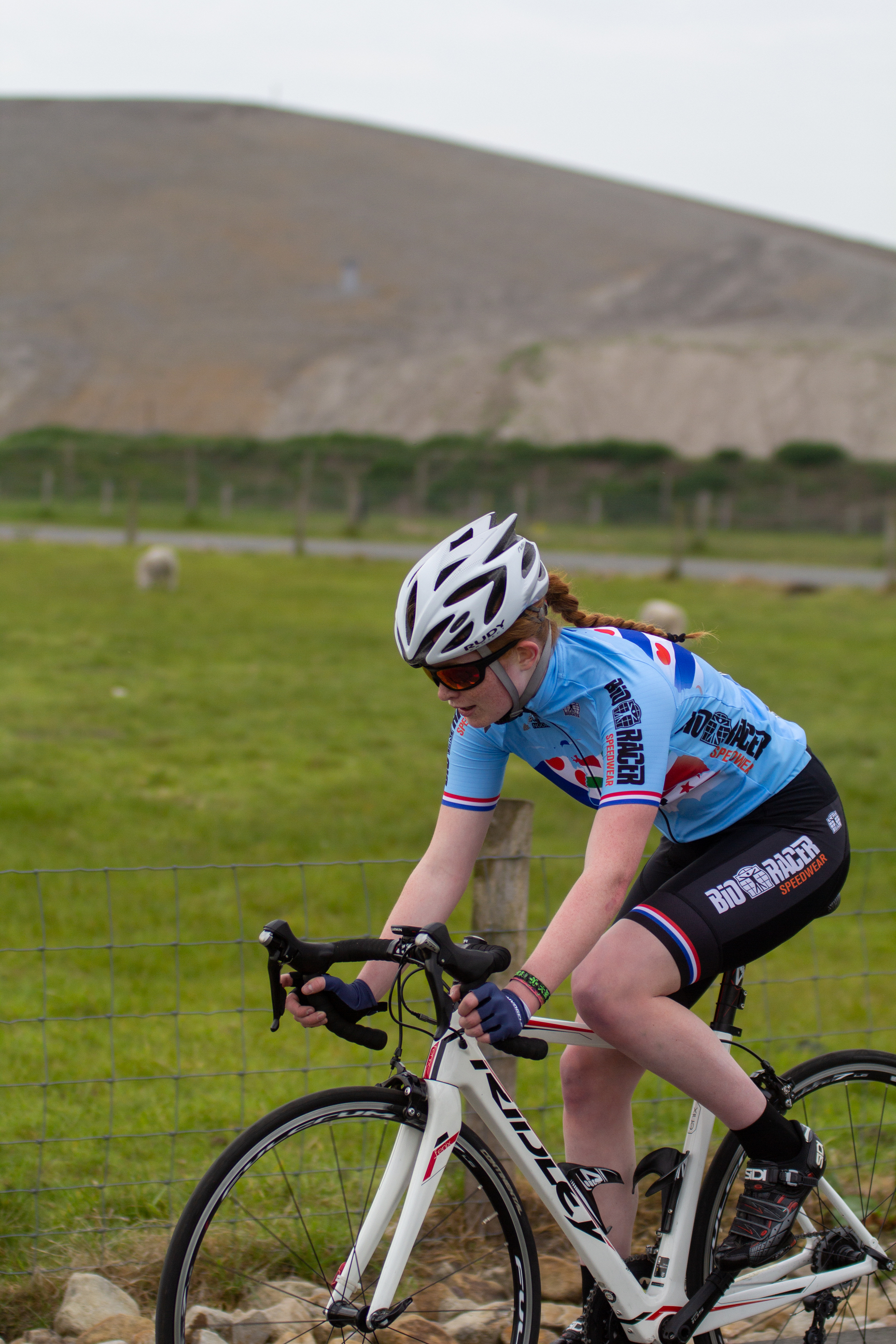 A woman is riding a bicycle while wearing the number 2 and has a helmet on.