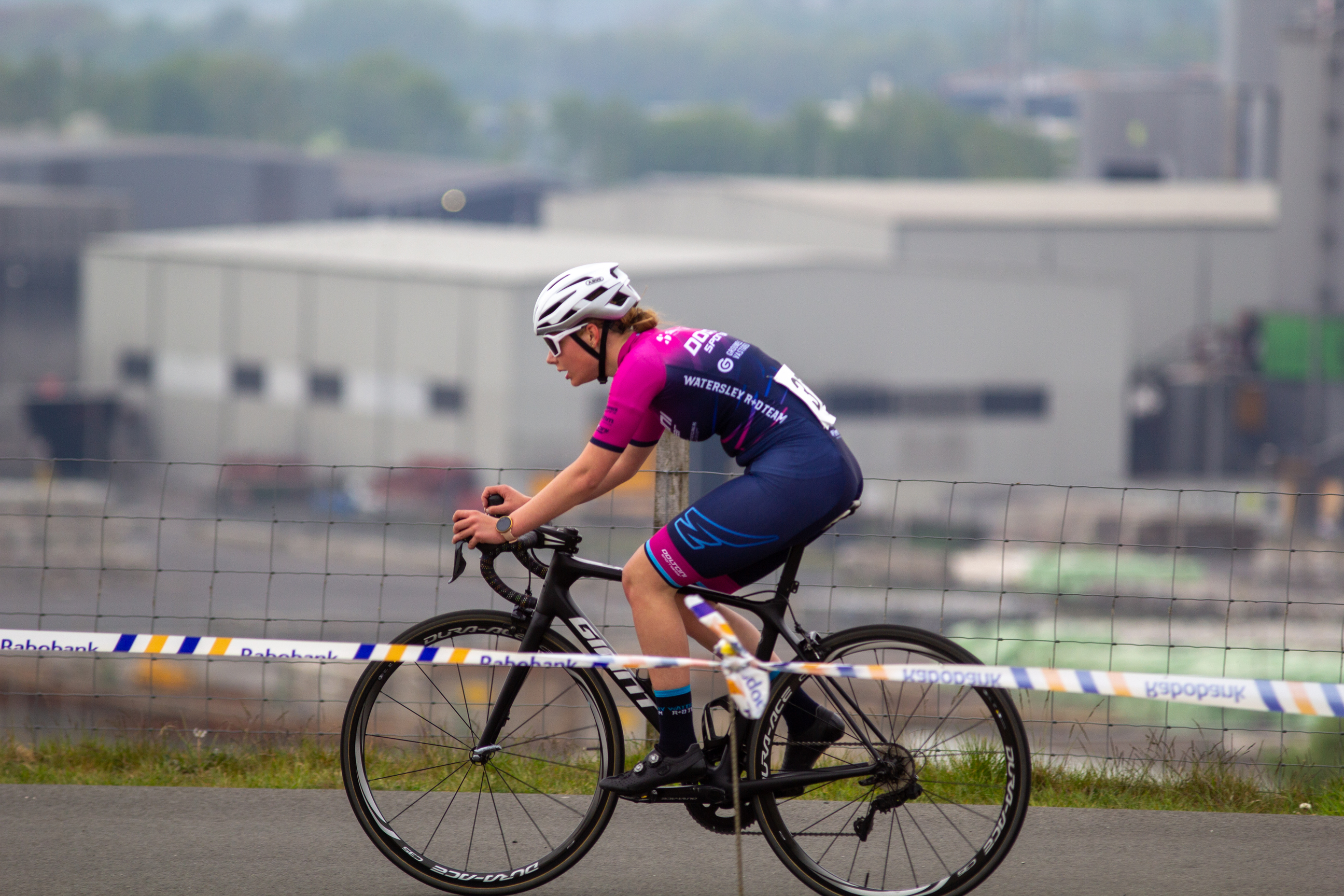 A female bicycle racer named Emily on a black bike with blue and pink clothing.