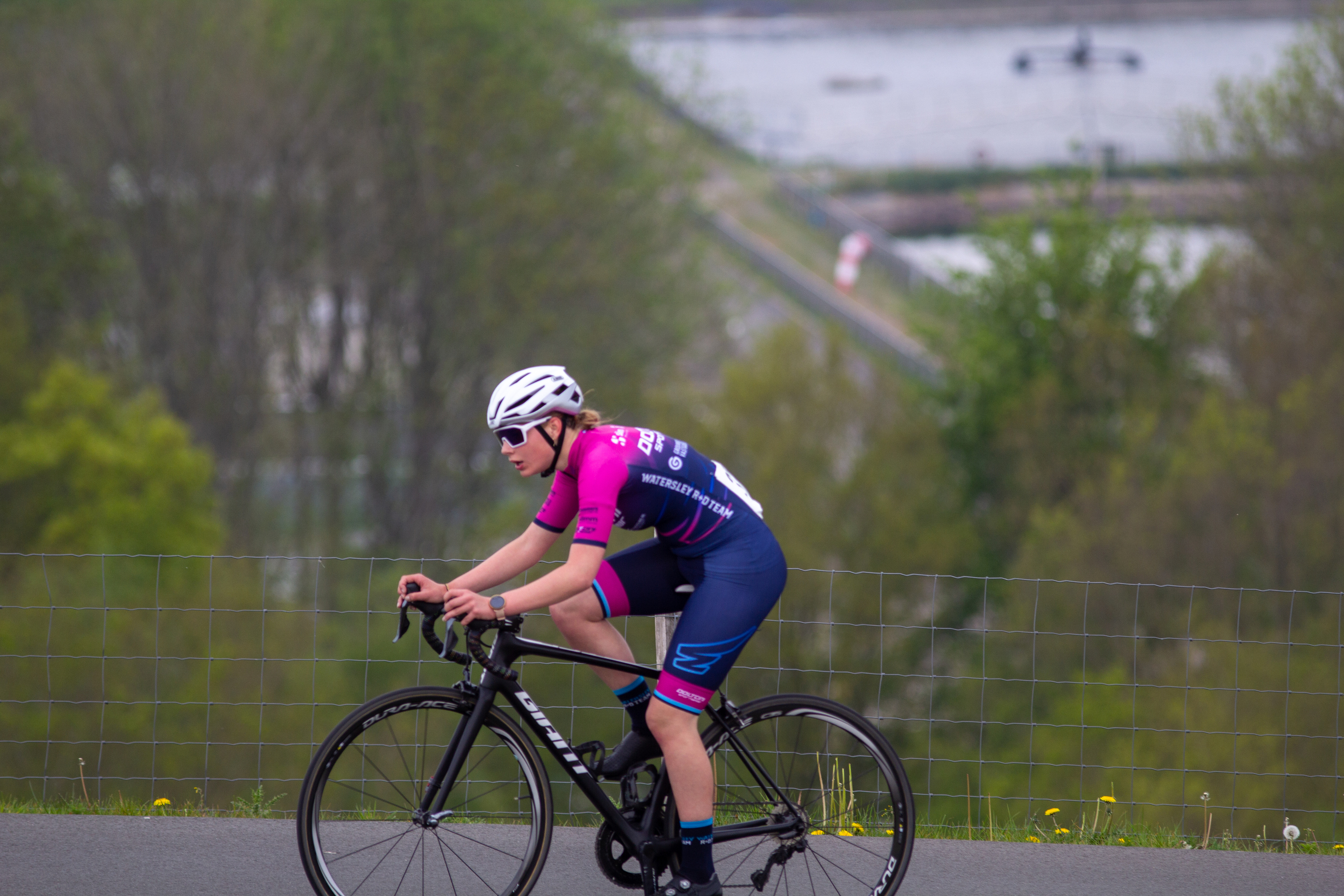 A young woman is riding a black bicycle on a trail while wearing a pink and blue top.