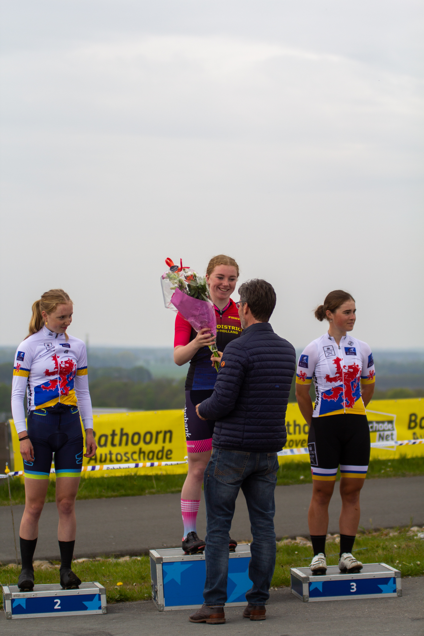 Three women are posing with their bicycles, one of them holding a bouquet.