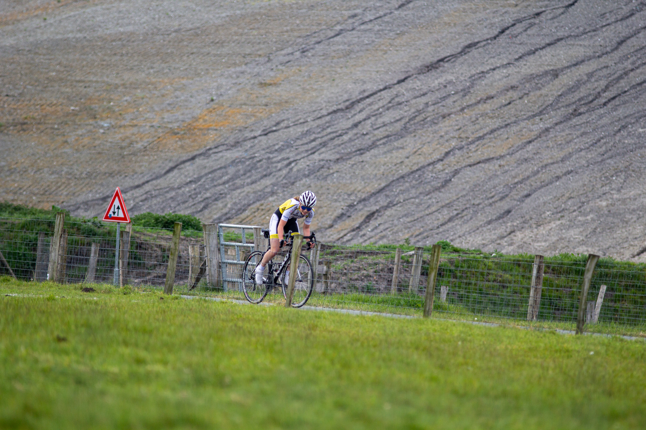 A cyclist racing on the course of Luge and the surrounding green grassy terrain.