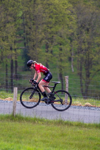 A female cyclist wearing a red top and black shorts riding a black bike.