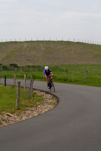 A cyclist wearing a white helmet is riding a black bicycle on a curvy road.