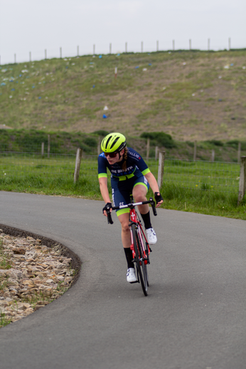 A woman in a blue and black cycling outfit is riding her bike on the road.