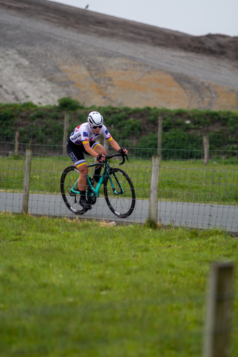 "A cyclist riding a bike on a track while wearing a helmet and jersey that says 'Dames'.