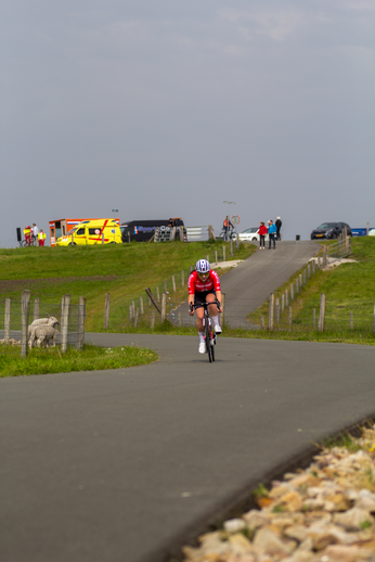 A woman in a red shirt and blue helmet riding a bicycle down the road.