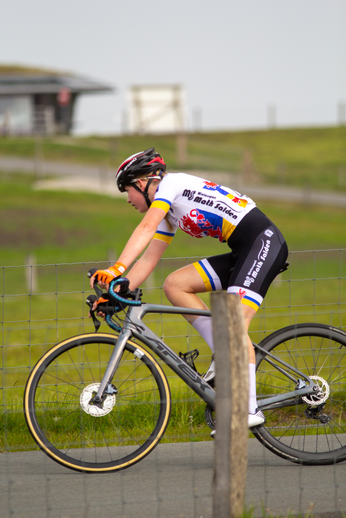 A woman in a blue, red and yellow jersey riding a bicycle.