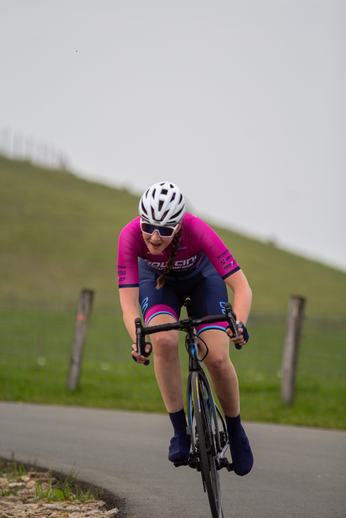 A woman wearing a pink bike jersey with the words "Giant" written on it, is riding a bicycle.