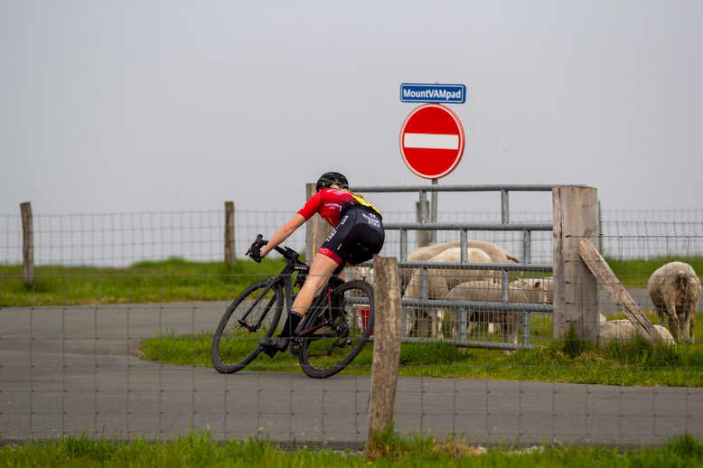 A woman in a pink and black uniform riding a bike with the words "Dames TT" on her back.