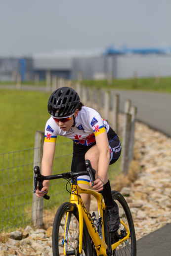 A woman wears a white jersey with Canadian flags and the words "Dames TT" across the front as she rides her yellow bike.