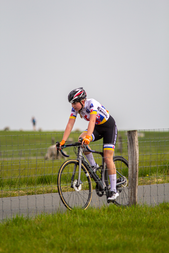 A woman wearing a white shirt with rainbow stripes and black shorts riding a bicycle.