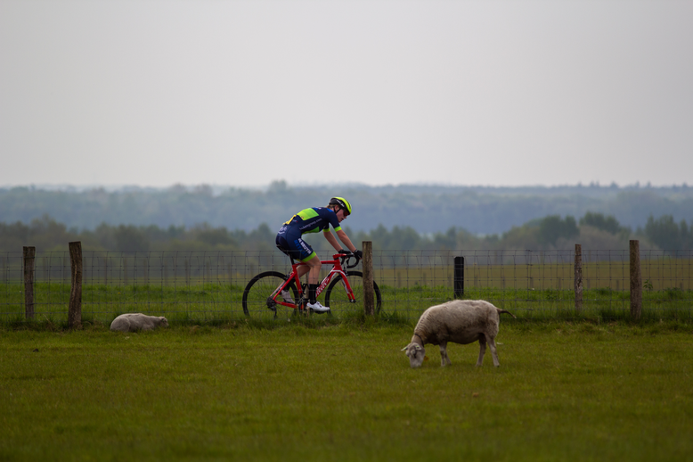 A man on a bike is following a woman, behind a fence.