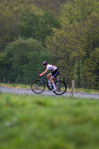 A cyclist in a black and white uniform races down a paved path.