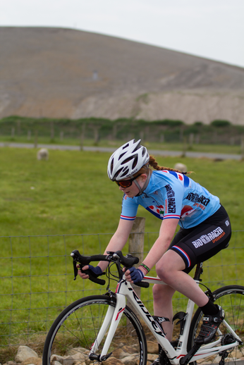 A woman is riding a bicycle while wearing the number 2 and has a helmet on.