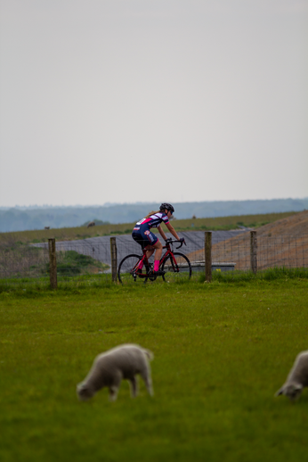 A woman wearing a blue outfit with the number 3 on it is riding her bike in a grassy field.