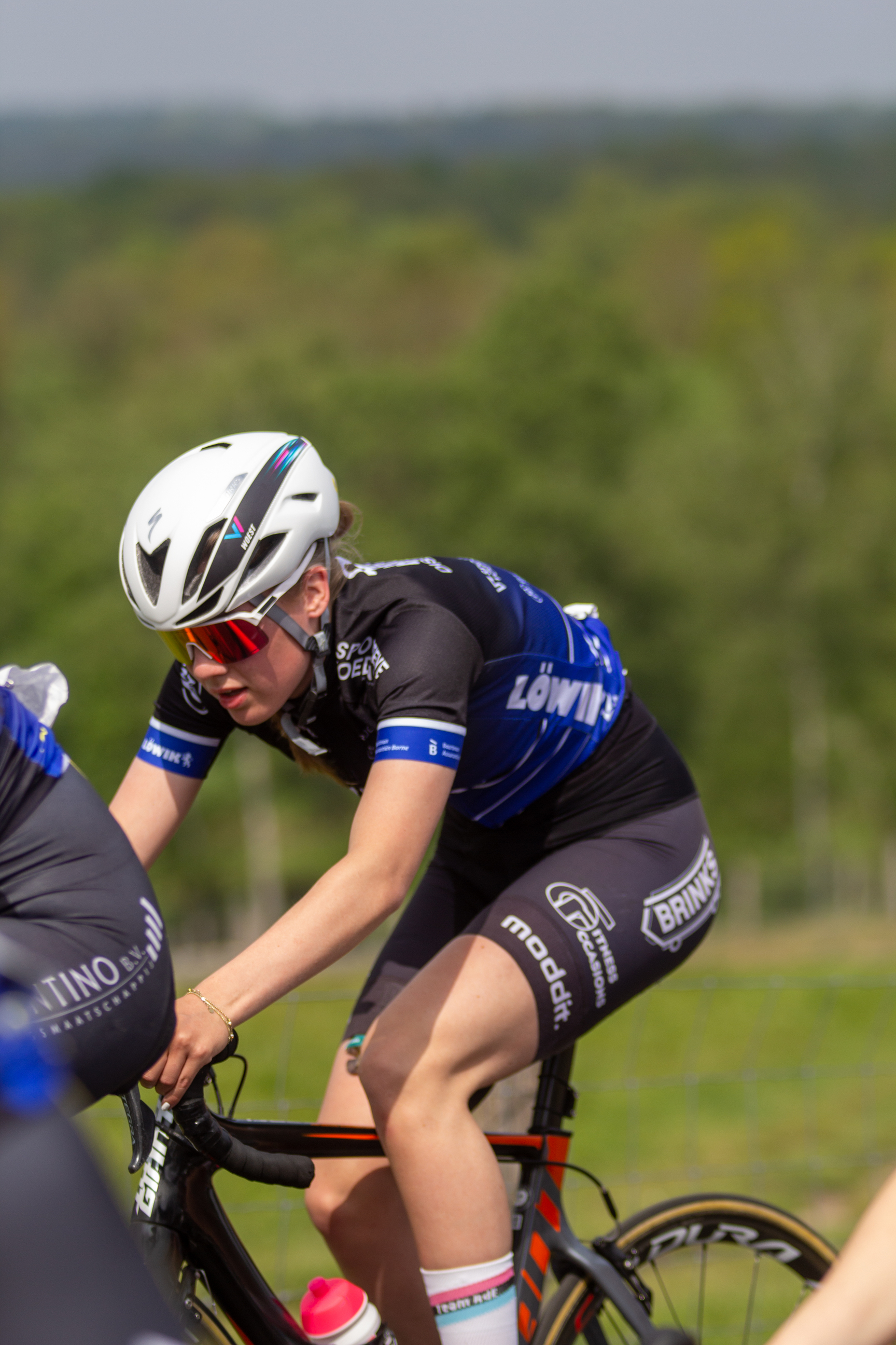 A girl in a blue and black uniform is wearing a helmet while riding her bicycle.