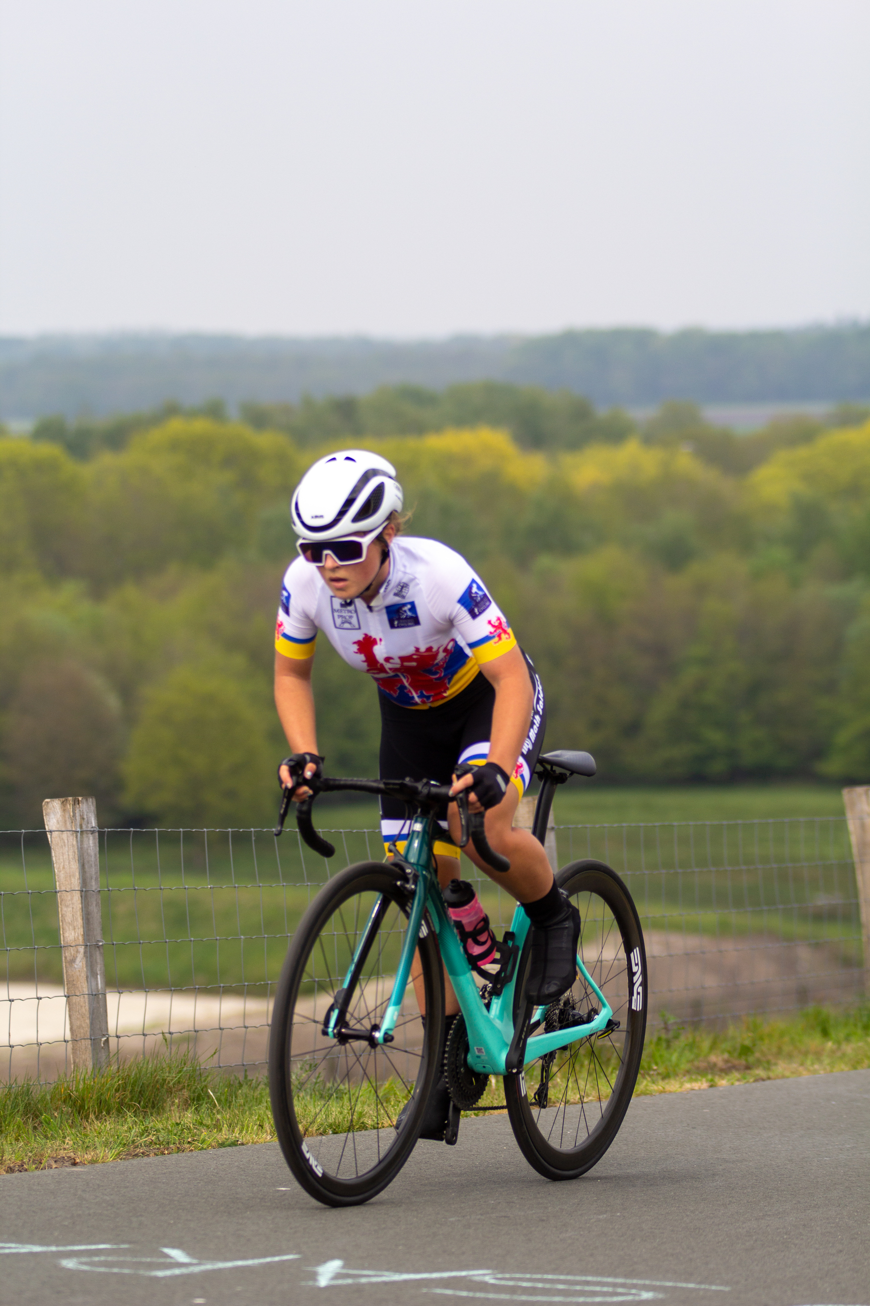 A female cyclist is wearing a white helmet and riding on the road.