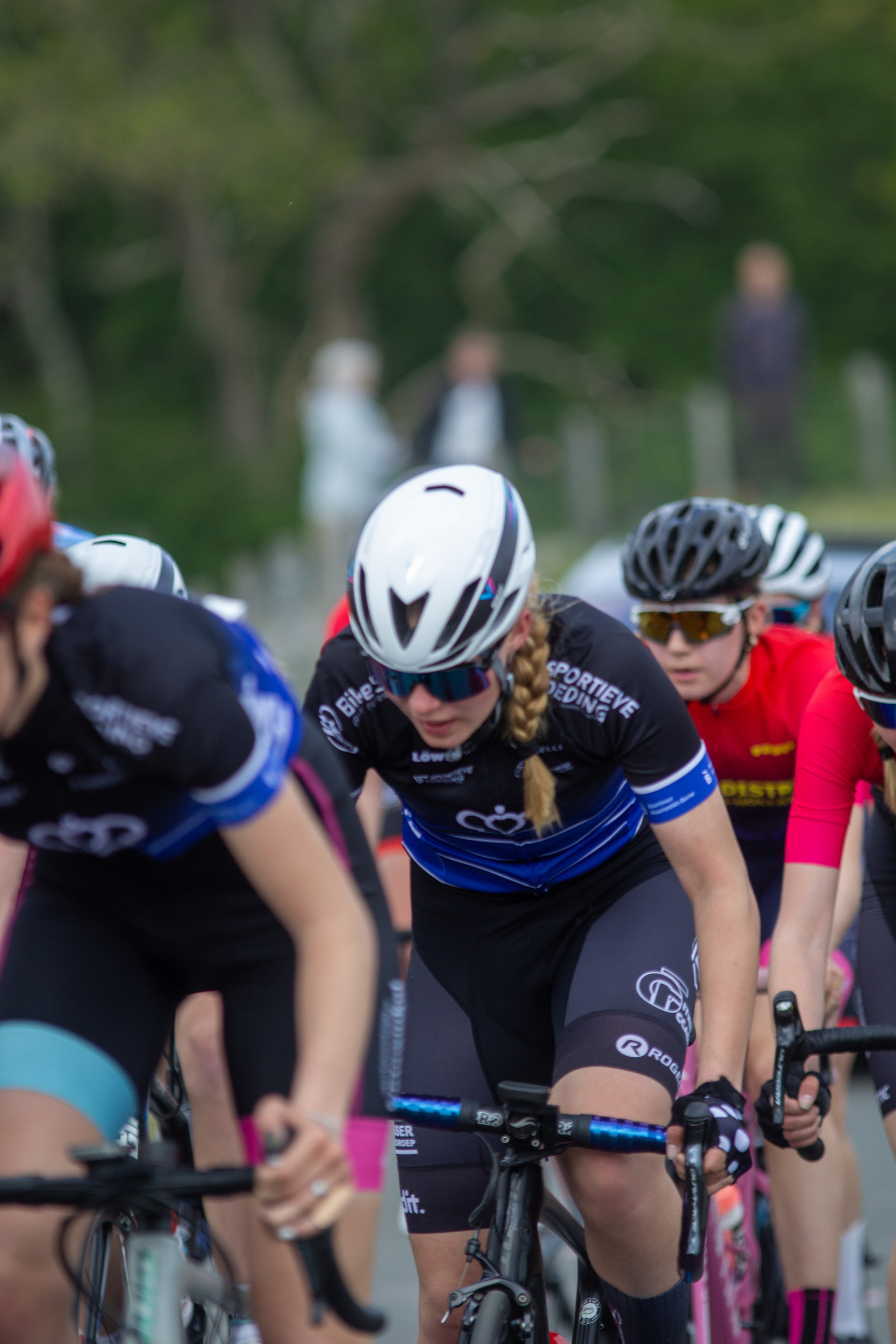 A group of cyclists race in a competition with several of them wearing helmets.