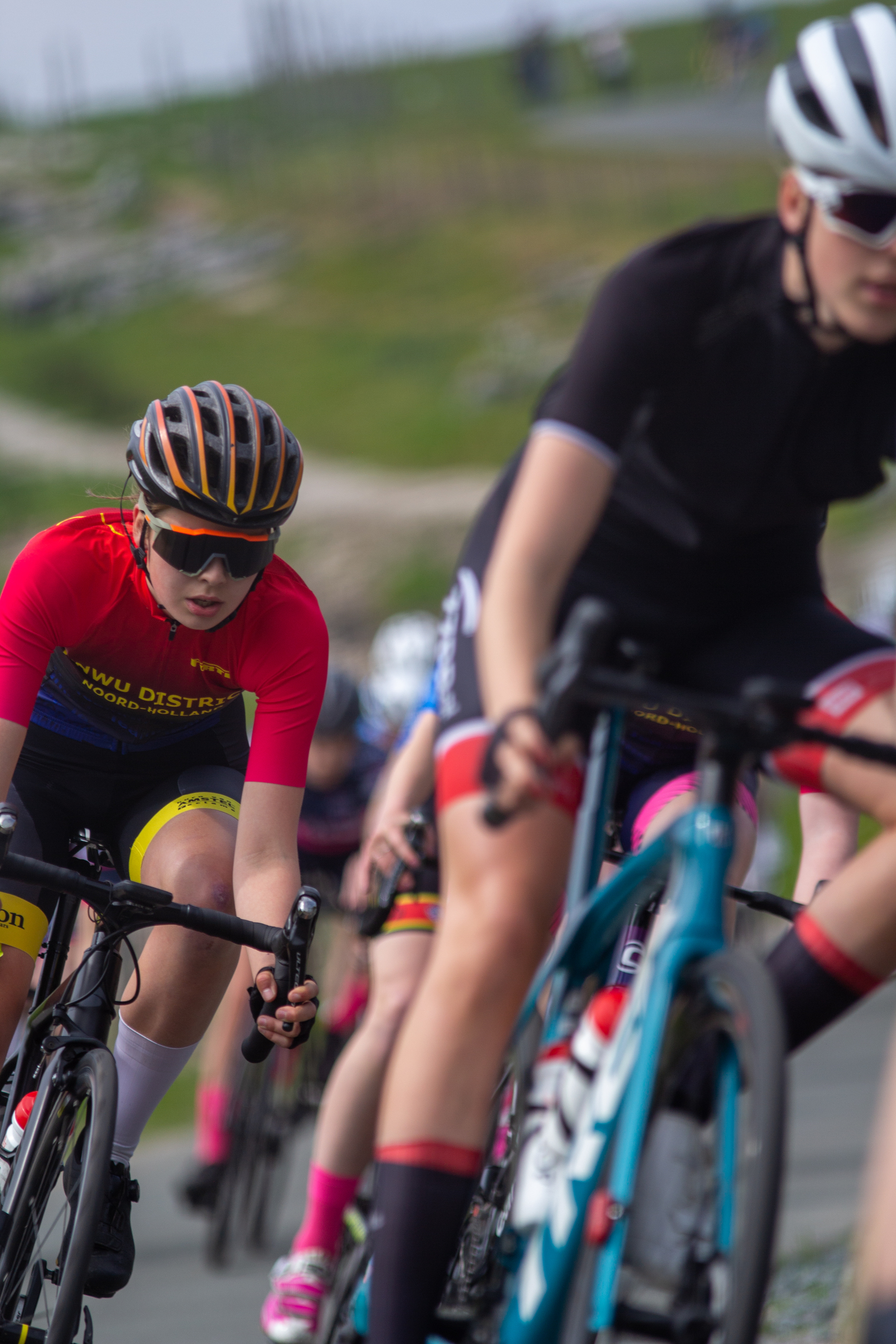 A group of female cyclists participating in the Tweedaagse Dames Criterium, riding on a road with pink and black shoes.