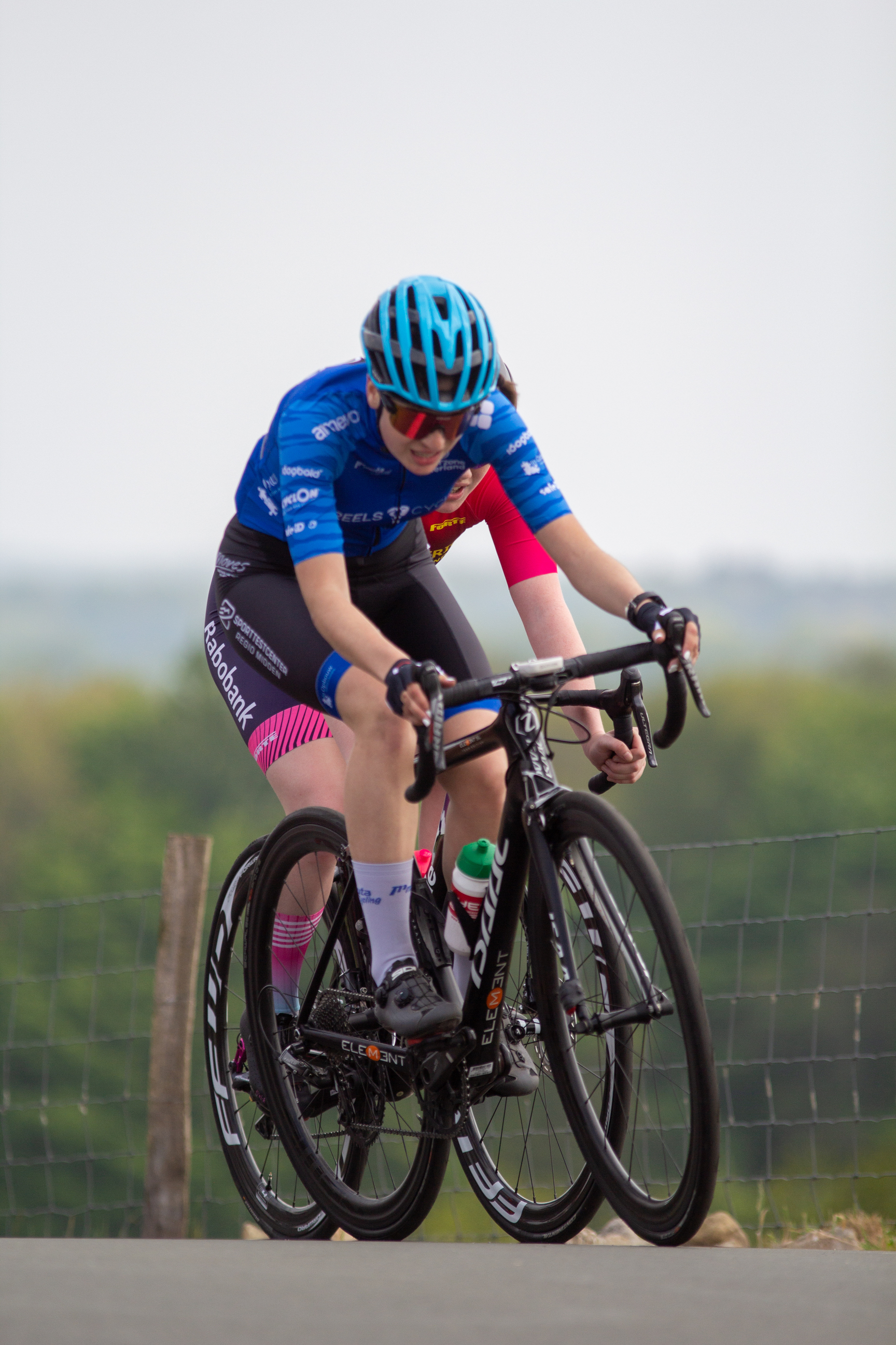 A young man wearing a blue helmet and jersey is riding a black bicycle.