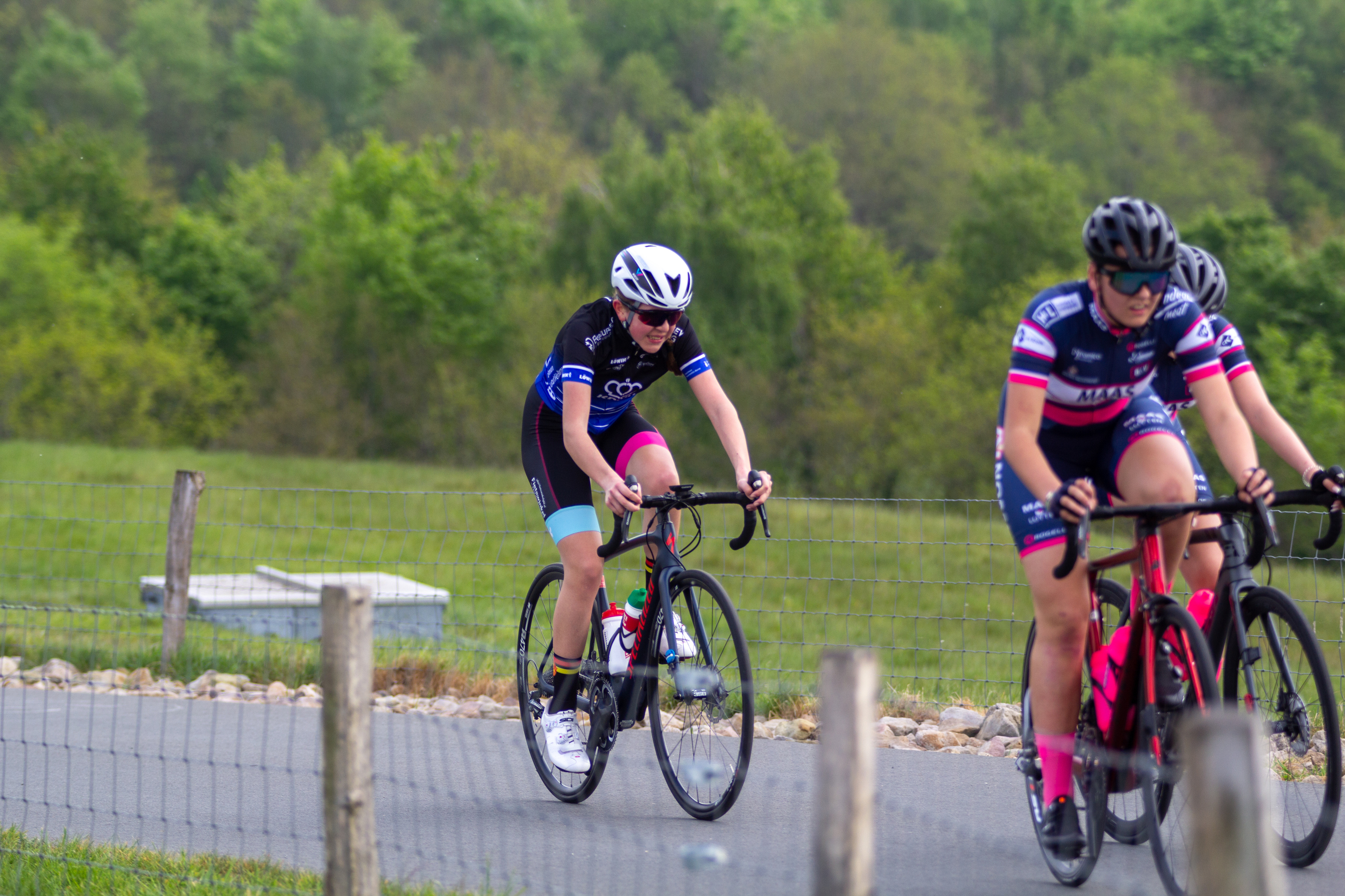 Two women on bicycles wearing pink and blue cycling suits compete in the Dames Criterium.