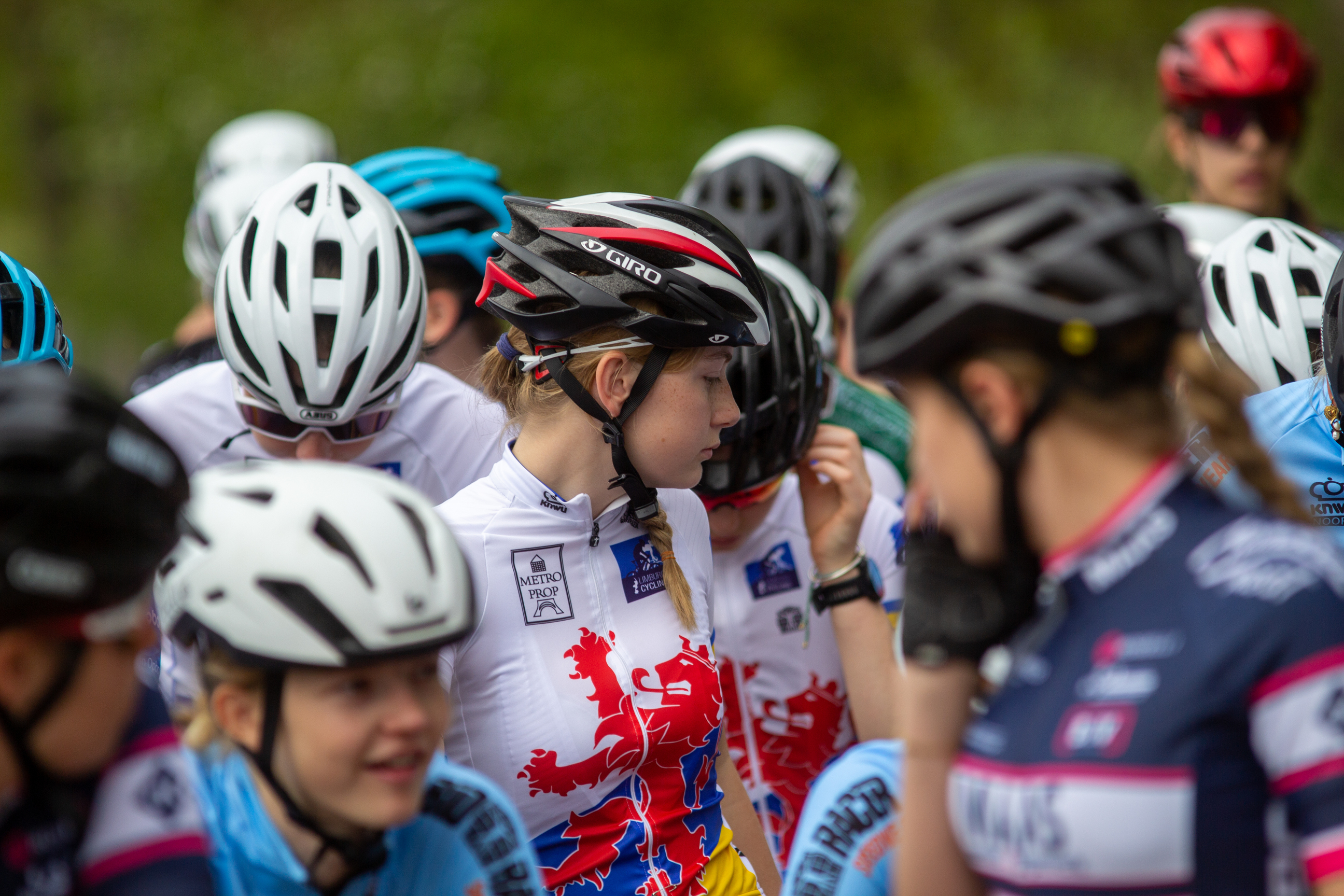 Group of athletes wearing helmets and race numbers are participating in the Dames Criterium Wielrennen event.