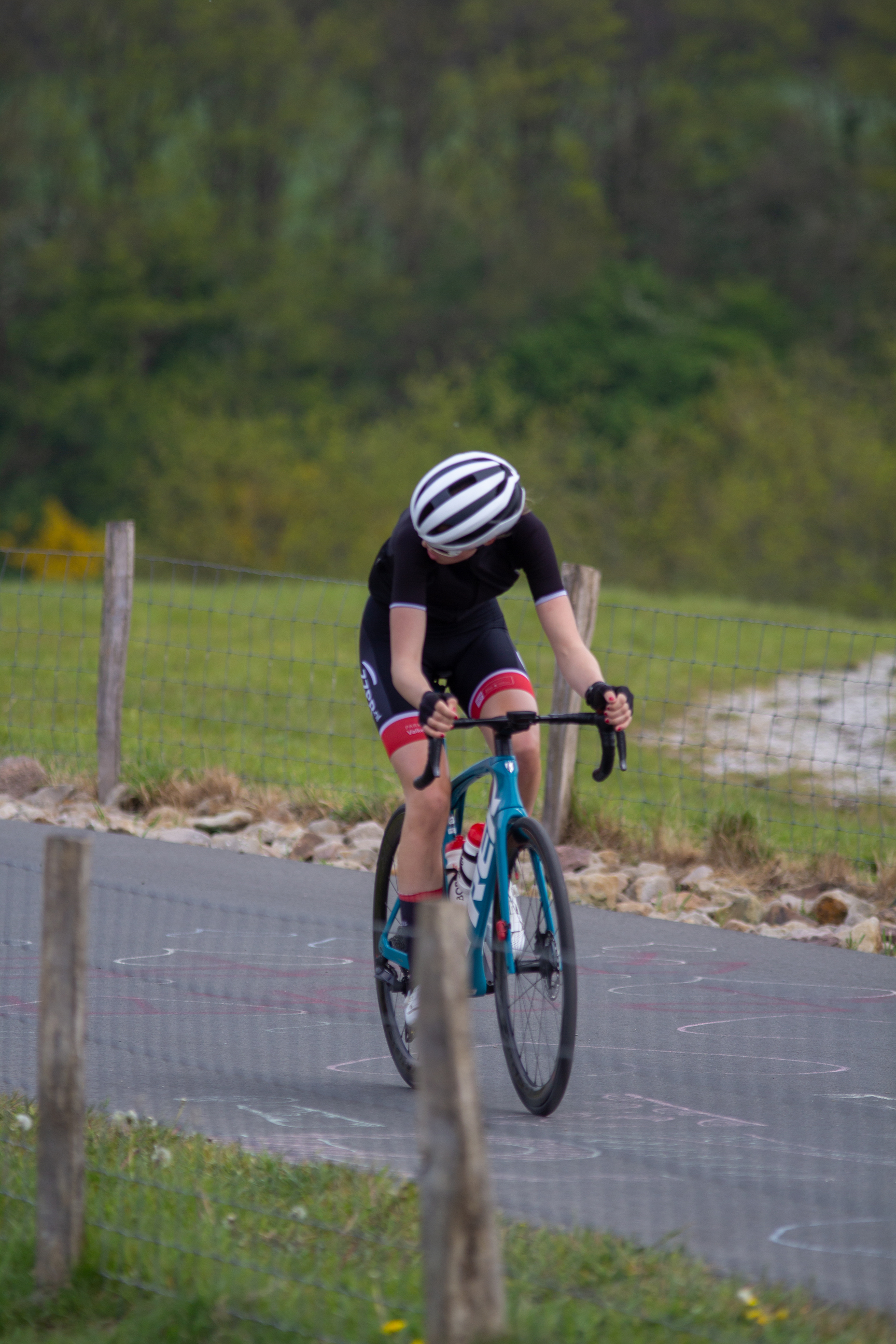 A cyclist in a black and white jersey is riding a blue bike.