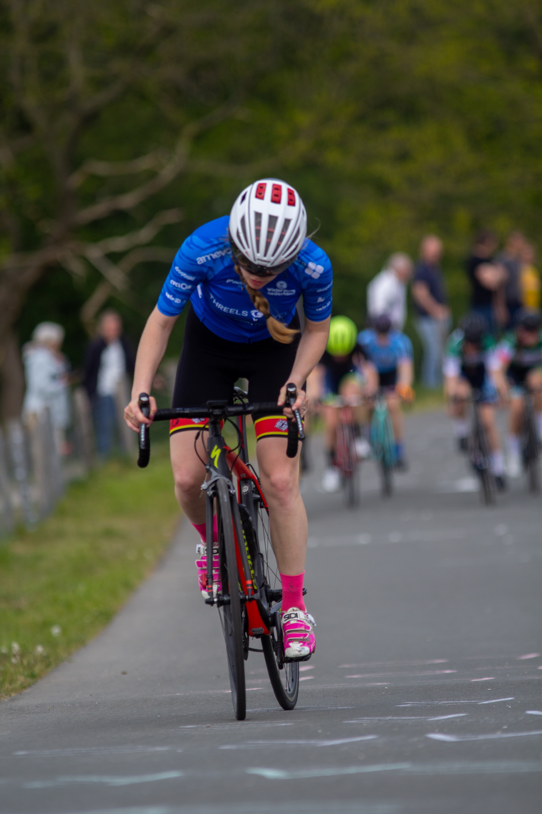 A woman in a blue shirt and pink shorts is riding her bicycle in a race.