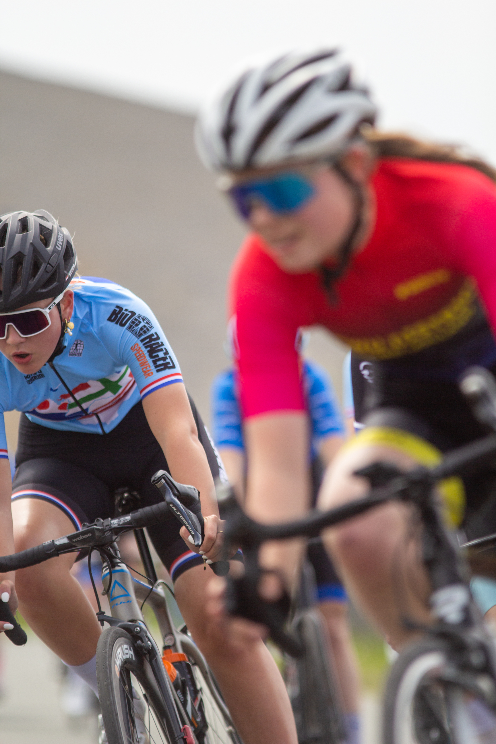 Two female cyclists race on a track with the words "Dames Criterium" displayed in the background.